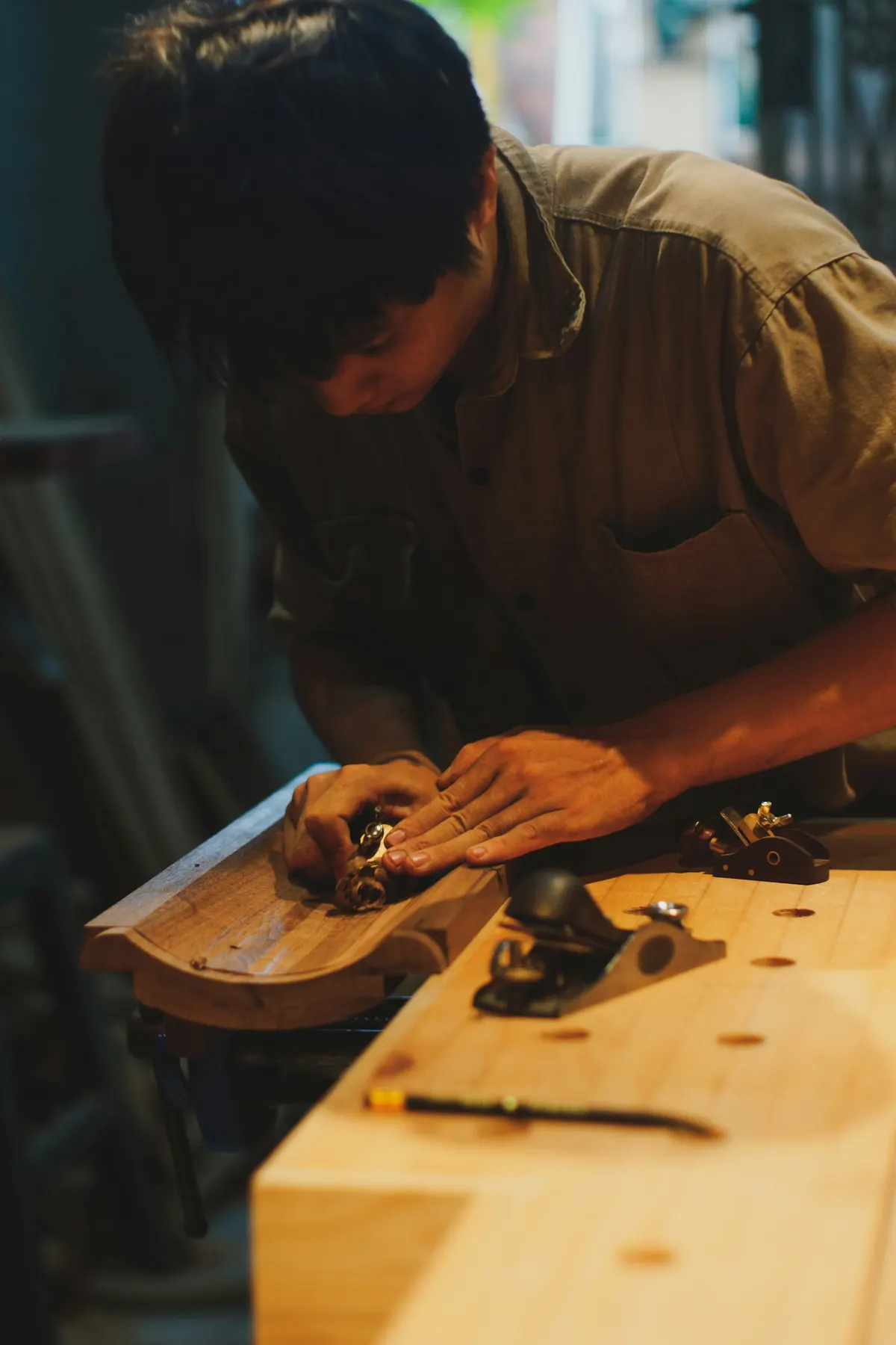 Des mains passent un rabot sur une pièce de bois, à l’atelier