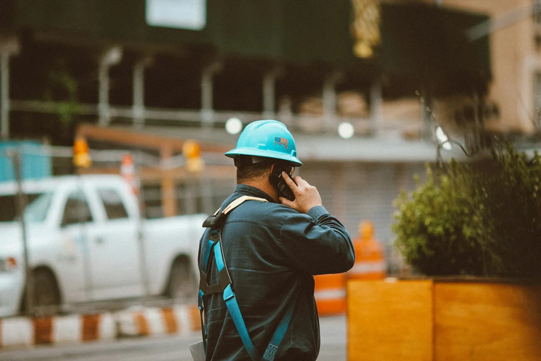 Un ouvrier casqué téléphone sur un chantier, vu de dos