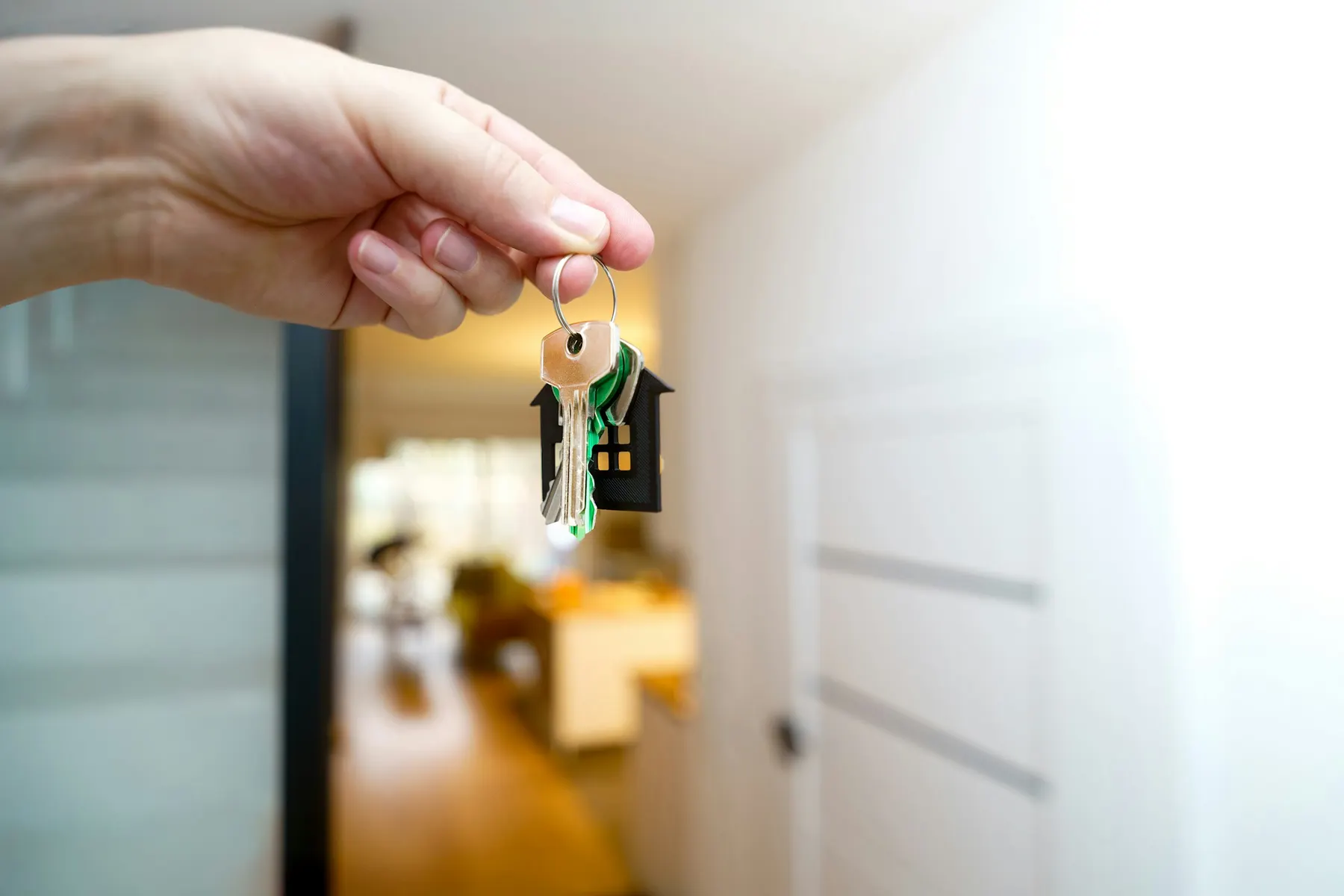 Une main tend un trousseau de clés dans l’entrée d’un appartement lumineux